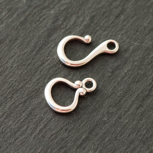 Puede incluir: Dos cierres de gancho plateados. Cada cierre tiene un cuerpo curvo en forma de U con una pequeña bola en la parte superior y un lazo en el extremo. Los cierres están diseñados para la fabricación de joyas o manualidades similares.