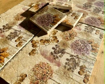 May include: A collection of square ceramic tiles with a floral design. The tiles feature a cream-colored background with a pattern of dried flowers in shades of brown, purple, and orange. Some tiles are stacked on top of others.