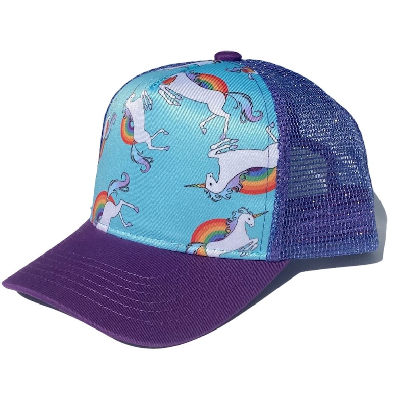 May include: A blue and purple trucker hat with a rainbow and unicorn print. The hat has a mesh back and a solid purple front.