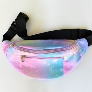 May include: A pink, blue, and green fanny pack with a galaxy print. The fanny pack has a black adjustable strap and a zipper closure.