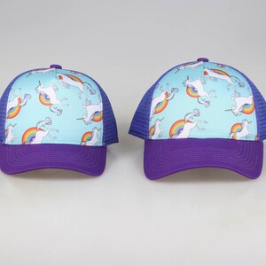 May include: Two purple and blue trucker hats with a light blue crown and a white unicorn and rainbow pattern.