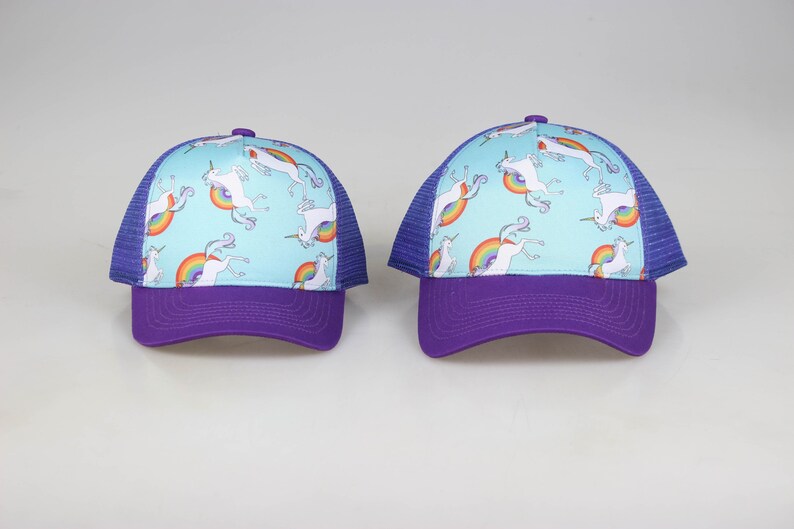 May include: Two purple and blue trucker hats with a light blue crown and a white unicorn and rainbow pattern.