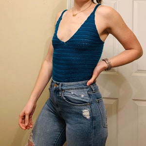 May include: A teal blue crochet tank top with a V-neckline. The tank top is worn with blue jeans.