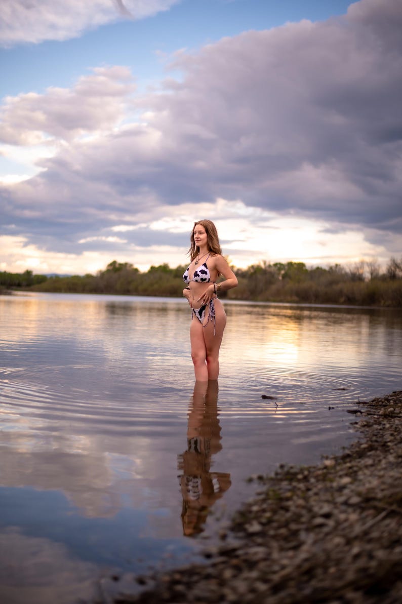 May include: A two-piece bikini set featuring a black and white cow print pattern. The top is a classic triangle style with thin straps, and the matching bottom features side-tie closures. The swimwear is constructed from a lightweight fabric.
