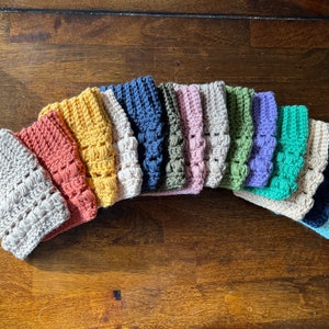 May include: A collection of 14 crocheted boot cuffs in various colors, including beige, orange, yellow, blue, green, purple, and teal.