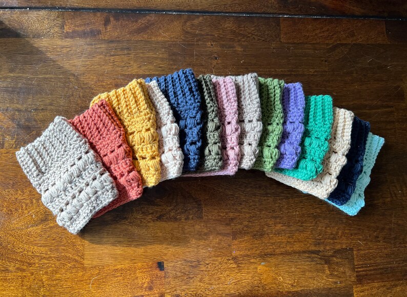 May include: A collection of 14 crocheted boot cuffs in various colors, including beige, orange, yellow, blue, green, purple, and teal.