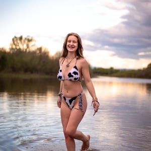 May include: A two-piece crochet bikini set featuring a white base with a black cow print pattern. The top is a classic triangle style with thin straps, and the bottom is a high-cut design with side ties, crafted from textured yarn material.