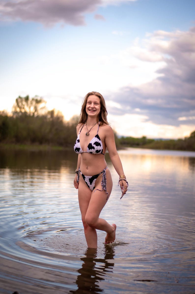 May include: A two-piece crochet bikini set featuring a white base with a black cow print pattern. The top is a classic triangle style with thin straps, and the bottom is a high-cut design with side ties, crafted from textured yarn material.