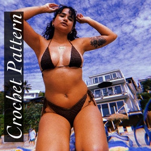 May include: A brown crochet bikini top and bottom with thin straps. The bikini is worn by a person with a tattoo on their arm. The person is standing on a beach with a blue sky and white clouds in the background.