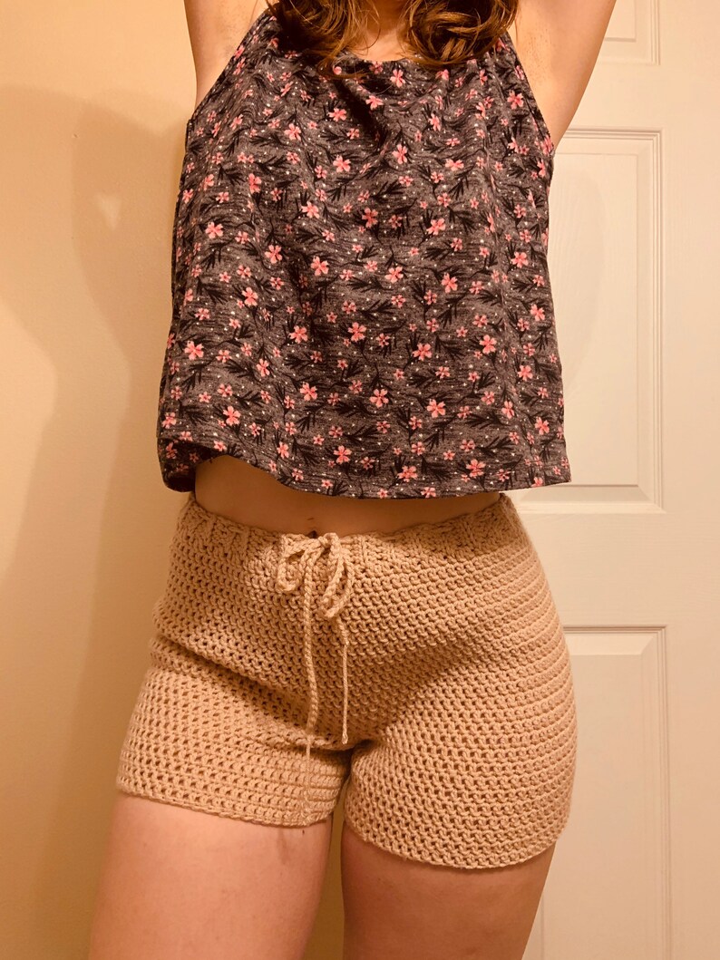 May include: Beige crochet shorts with a drawstring waist. The shorts are made with a textured stitch and are a loose fit.