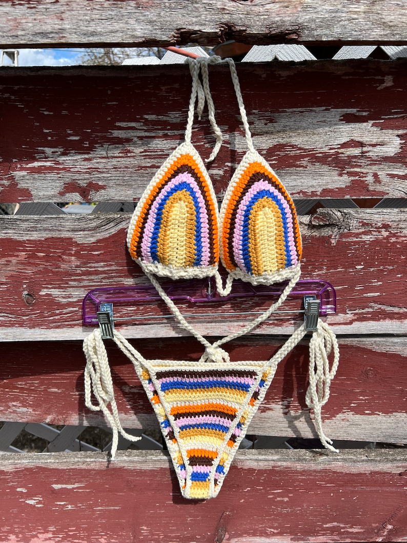 May include: A crocheted bikini top and bottom with a rainbow stripe pattern in shades of brown, orange, yellow, blue, pink, and white.