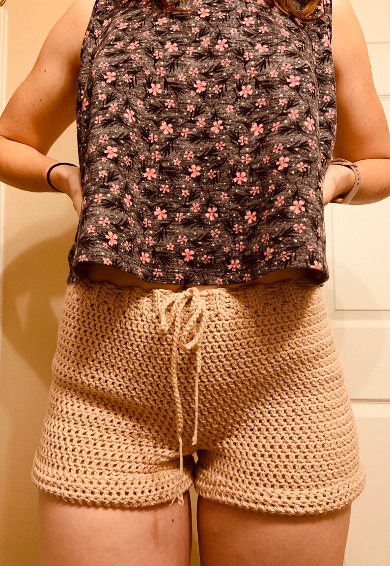 May include: Beige crochet shorts with a drawstring waist. The shorts are made with a simple stitch pattern and have a relaxed fit.