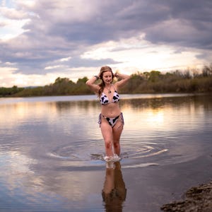 May include: A two-piece bikini set featuring a black and white cow print pattern. The top is a triangle style with thin straps, and the bottom is a classic cut with side ties. The swimwear is made of a smooth fabric with a consistent spotted design.