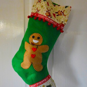 May include: Green Christmas stocking with a gingerbread man applique and a reindeer pattern on the top and bottom. The stocking has red pom-poms and a red ribbon with the text "Merry Christmas".