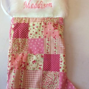 May include: A festive Christmas stocking with the name "Maddison" embroidered in pink on a white faux fur cuff. The body is a patchwork of pink floral and polka dot fabrics, a charming holiday decoration.