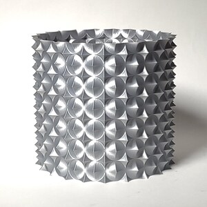 May include: A silver cylindrical vase with a geometric pattern of raised circles and points.