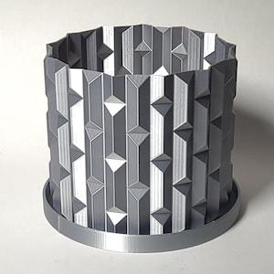 May include: A gray 3D printed planter with a geometric design. The planter has a wide base and a cylindrical shape.