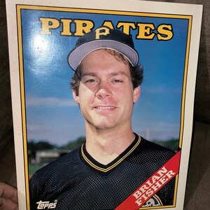 May include: A vintage Topps baseball card featuring Brian Fisher of the Pittsburgh Pirates. The card has a yellow border with the team name "PIRATES" at the top. Fisher is wearing a black and gold jersey and a baseball cap.