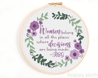 May include: Cross stitch pattern featuring a floral wreath with purple flowers and green leaves. The quote "Women belong in all the places where decisions are being made. ~RBG" is stitched in the center.