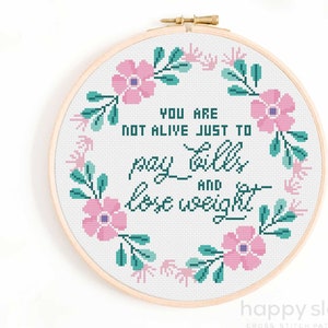 May include: A white embroidery hoop with a floral wreath design and the text "You are not alive just to pay bills and lose weight".