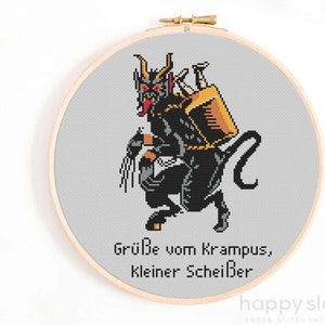 May include: Cross stitch pattern featuring a black and red Krampus with a sack on his back. The text below reads "Grüße vom Krampus, kleiner Scheißer".
