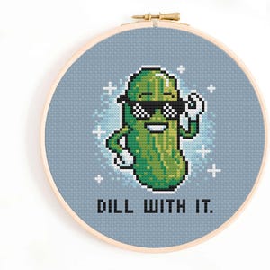 以下が含まれることがあります： 「DILL WITH IT.」というテキストと、サングラスと帽子をかぶった緑色のピクルスのクロスステッチパターンです。