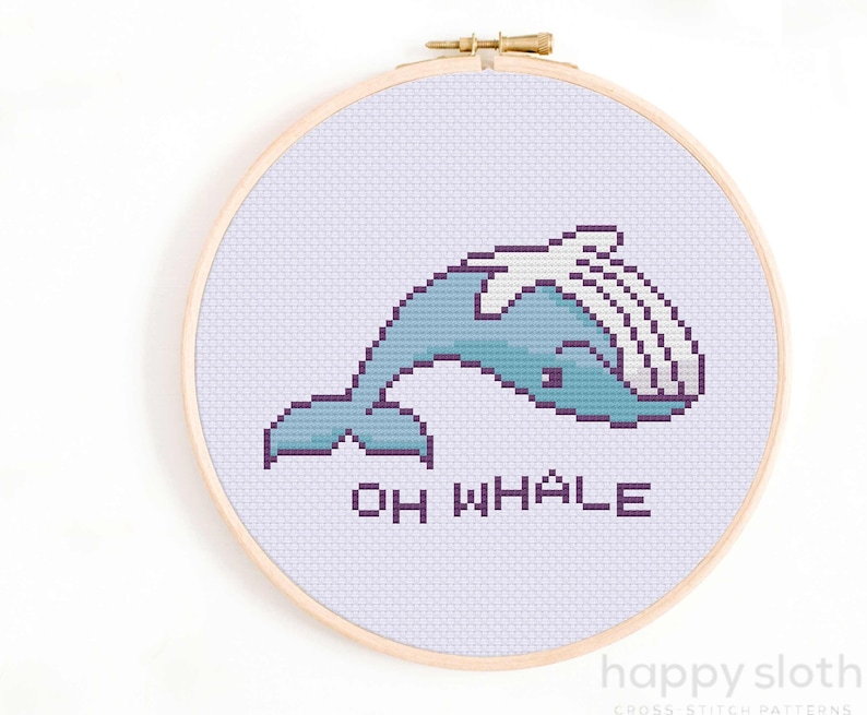 May include: Cross stitch pattern featuring a cartoon whale with the text "Oh Whale" in purple lettering. The whale is blue and white and is stitched on a light purple background.