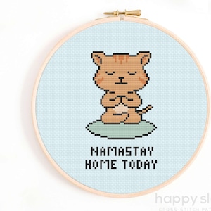 May include: Cross stitch pattern featuring a cartoon orange cat meditating with the text "namasstay home today" on a light blue background.
