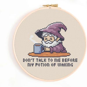 Puede incluir: Un patrón de punto de cruz con un mago de dibujos animados con un sombrero morado y barba, sosteniendo una taza. El texto dice "No me hables antes de mi poción de despertar."