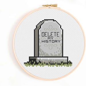 May include: A cross-stitch pattern of a tombstone with the text "DELETE MY HISTORY" on it. The tombstone is gray with a green grass base.