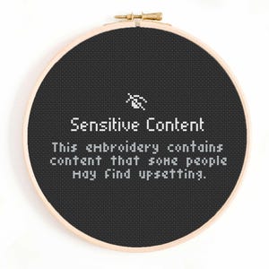 Può includere: Ricamo a punto croce in un telaio di legno. Il tessuto nero presenta un testo bianco che recita "Sensitive Content". Sotto, il testo continua: "This embroidery contains content that some people may find upsetting."