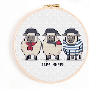 Könnte beinhalten: Ein Kreuzstich-Stickrahmen mit drei pixeligen Schafen, die Baskenmützen tragen. Ein Schaf hat einen roten Schal, ein anderes hält eine rote Rose und das dritte trägt ein blau-weiß gestreiftes Hemd. Der Text "TRÈS SHEEP" steht darunter.
