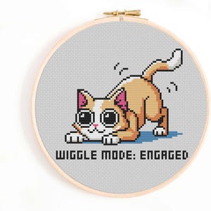 May include: Cross stitch pattern featuring a cartoon cat with big eyes and the text "Wiggle Mode: Engaged".