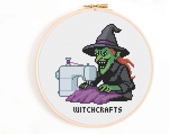 Può includere: Ricamo a punto croce in un telaio di legno. Il disegno presenta una strega dalla pelle verde con cappello e cappotto neri, che cuce con una macchina da cucire. Il testo "WITCHCRAFTS" è sotto.