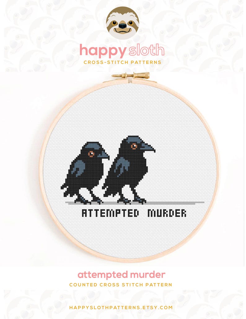Puede incluir: Patr&oacute;n de punto de cruz con dos cuervos negros con ojos naranjas, uno al lado del otro. La frase "ATTEMPTED MURDER" est&aacute; debajo de los p&aacute;jaros. El dise&ntilde;o est&aacute; en un bastidor de bordado de madera, con el logotipo de Happy Sloth en la parte superior.