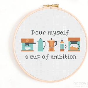 Peut inclure: Un cerceau de broderie blanc avec un motif de point de croix de cafetières et le texte "Pour myself a cup of ambition."