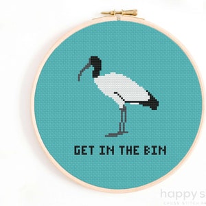 Puede incluir: Un patrón de punto de cruz con un ibis blanco con cabeza y pico negros, de pie sobre un fondo turquesa. El texto "GET IN THE BIN" está escrito debajo del pájaro.