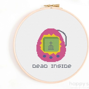 May include: Cross stitch pattern of a pink Tamagotchi with a green screen displaying a tombstone and the text "dead inside".