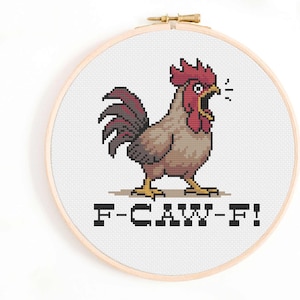 May include: A cross-stitch embroidery hoop featuring a pixelated rooster with a red comb and tail, and a brown body. The rooster is open-mouthed, with the text "F-CAW-F!" below it. The hoop is made of wood.