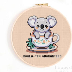 May include: A cross-stitch pattern featuring a cute gray koala sitting in a teacup with a floral design. The text "Koala-tea Guaranteed" is below the image.