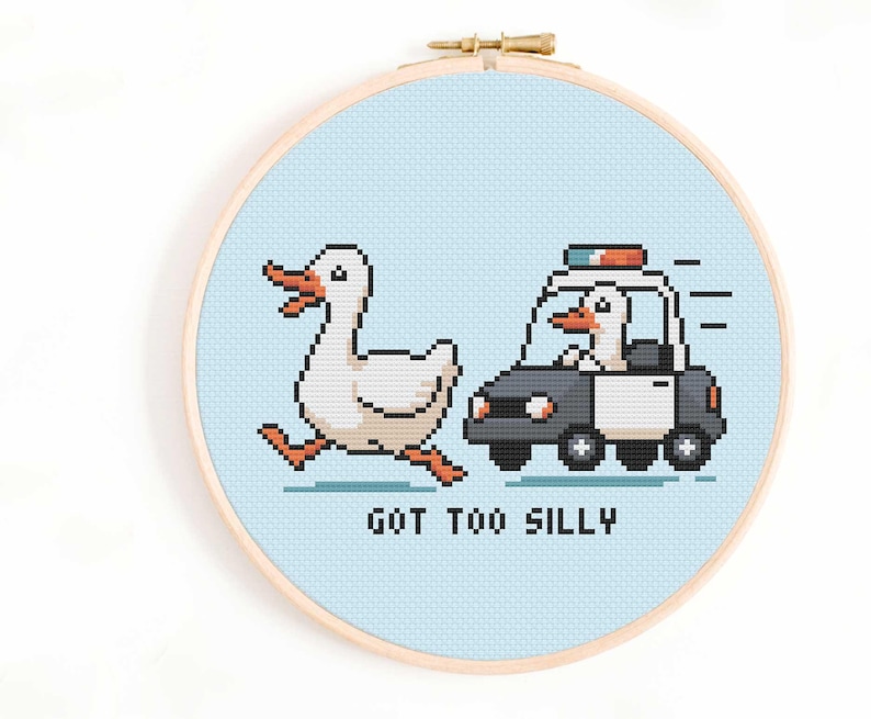 May include: A cross-stitch hoop featuring a pixelated design of a white duck running from a police car driven by a duck. The text "GOT TOO SILLY" is below the car. The background is light blue.