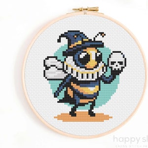 May include: Cross stitch pattern of a bee wearing a witch's hat and holding a skull. The bee is yellow and black with blue wings. The background is a light blue circle.