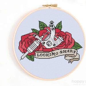 May include: Cross stitch pattern featuring a tattoo machine with a red rose and a banner that reads "Looking Sharp".