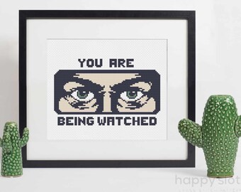 May include: A cross stitch pattern featuring a pair of eyes with the text "You are being watched" in black and white.