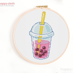 May include: A cross-stitch pattern of a pink bubble tea with black tapioca pearls, a yellow straw, and a blue lid in a white plastic cup.