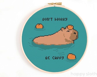 May include: Cross stitch pattern featuring a capybara swimming in turquoise water with the text "Don't worry, be capy" and three orange fruit on top of the capybara and in the water.