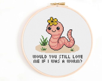 May include: Cross-stitch embroidery in a wooden hoop features a smiling pink worm wearing a yellow flower. The text reads, "WOULD YOU STILL LOVE ME IF I WAS A WORM?" Green grass and tan soil are also included in the design.
