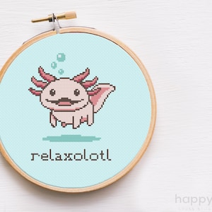 May include: A cross stitch project in a wooden embroidery hoop featuring a light pink pixel art axolotl on a light blue background with three bubbles above its head and the text relaxolotl stitched in black letters below the creature.