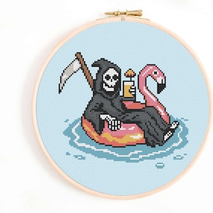 Op de afbeelding: Een kruissteekpatroon met een cartoon Grim Reaper die een zwarte robe draagt en een cocktail vasthoudt, drijvend op een roze flamingo zwemband. De Grim Reaper houdt een zeis vast op de achtergrond.