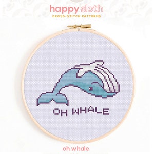 May include: Counted cross stitch pattern of a blue whale with the text "Oh Whale" in purple. The pattern is displayed in a wooden embroidery hoop.